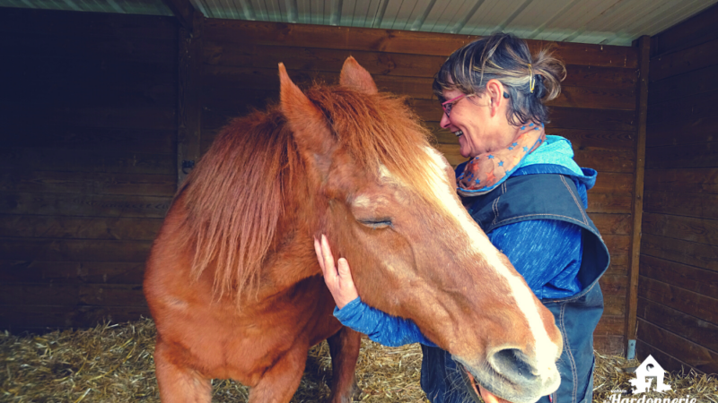 Une femme caresse un poney tout en souriant.